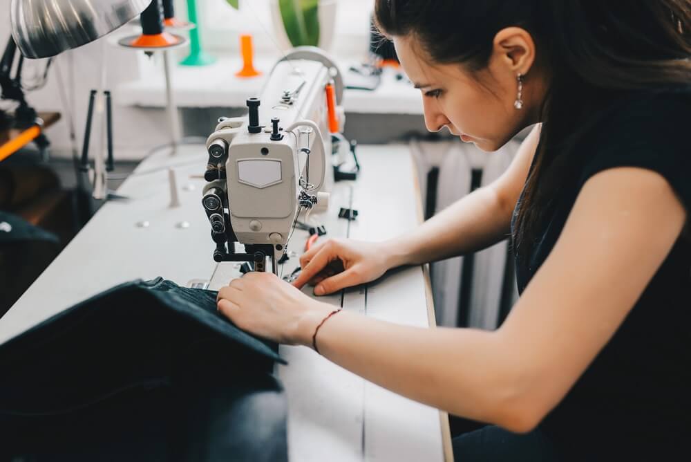 Female artisan threading black leather on sewing machine, close